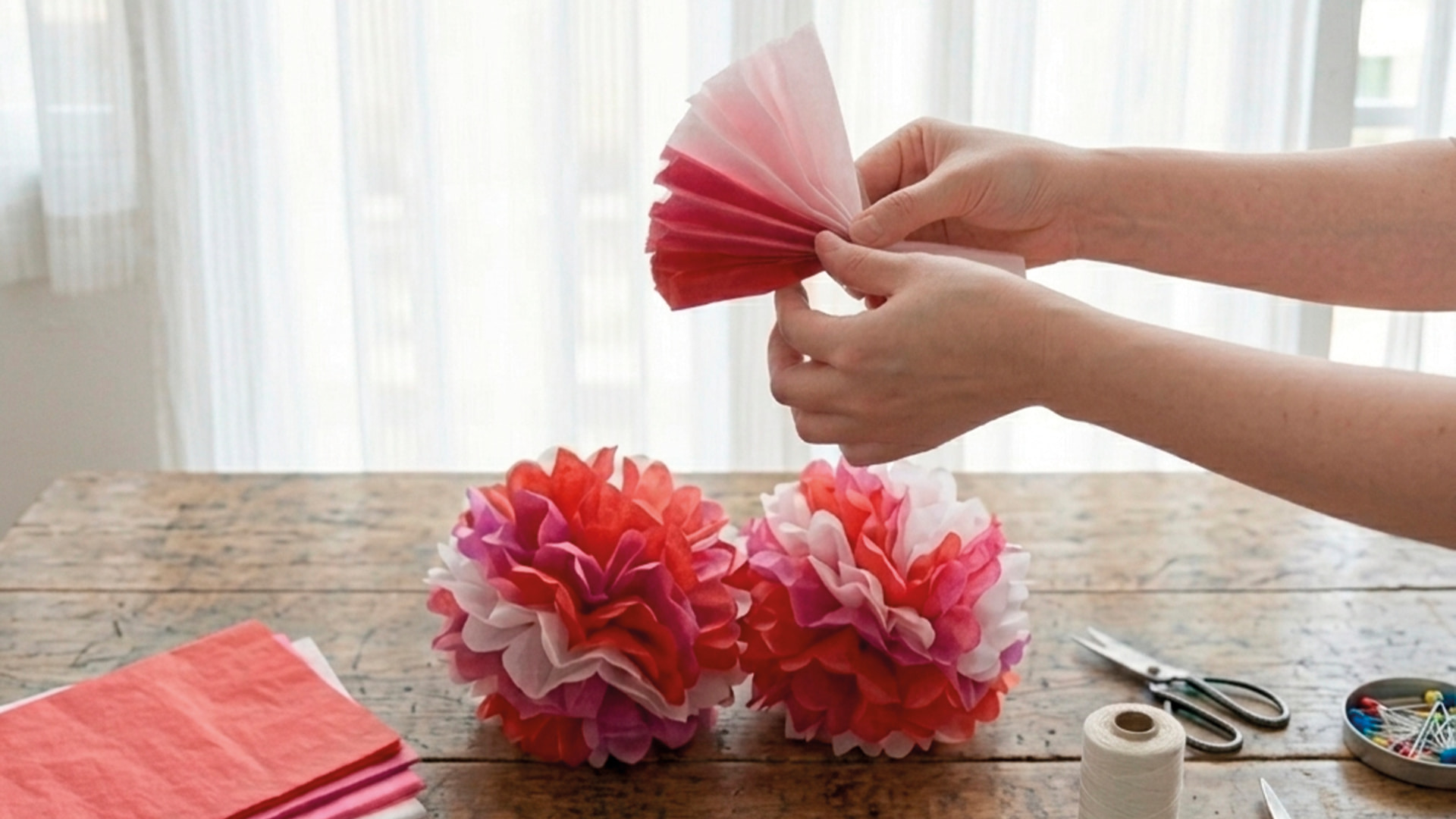 Mains créant des pompons décoratifs en papier de soie rose, rouge et blanc